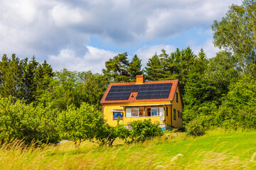 Obraz premium Beautiful yellow countryside house with solar panels on red roof surrounded by green trees and grass. Sweden.