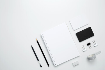 On a white background, an empty mock up notebook, white and black cards, monochrome stationery items arranged neatly