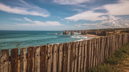 Obraz premium Vertical capture of a timber fence by the water and rocky coast