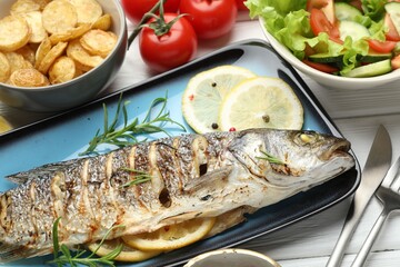 Tasty roasted seabass fish served with salad and potatoes on white wooden table, closeup. Homemade seafood dish