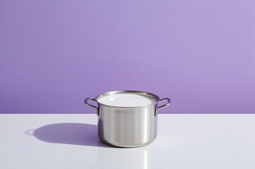 Light milk in a tiny saucepan against a violet backdrop with grainy texture