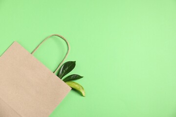 Eco friendly packaging. One paper bag and leaves on light green background, top view. Space for text