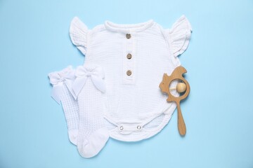 Stylish baby onesie and accessories on light blue background, flat lay