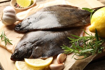 Fresh flounder fish, lemon, rosemary and garlic on wooden table, closeup. Raw seafood