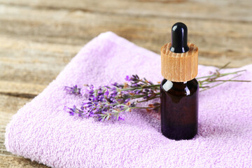 Lavender essential oil, flowers and towel on wooden table, closeup