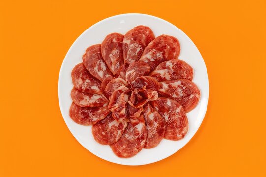 Sliced cured pork ham served on a plate against an orange backdrop, top-down view.