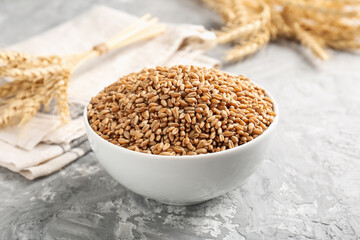Wheat grains in bowl and spikes on grey table, closeup