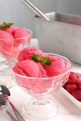 Delicious raspberry sorbet with mint in dessert bowls, spoons and fresh berries on white wooden table against light grey background, closeup