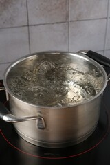 Metal pot with boiling water on stove in kitchen, closeup