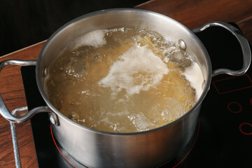 Fresh tagliatelle pasta boiling in pot with water on electric stove, closeup