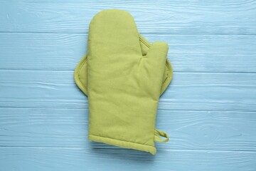 Green oven glove and potholder on light blue wooden table, top view