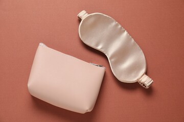 Cosmetic bag and sleeping mask on brown background, flat lay