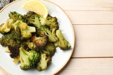 Tasty fried broccoli and lemon on light wooden table, top view. Space for text