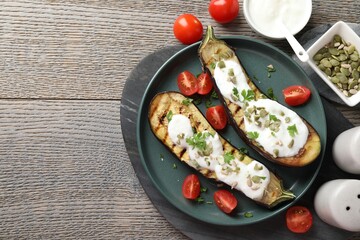Slices of grilled eggplant with pumpkin seeds, tomatoes and yoghurt on wooden table, flat lay. Space for text