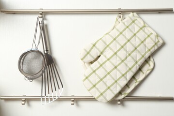 Oven glove, potholder and other kitchen utensils on metal rack indoors