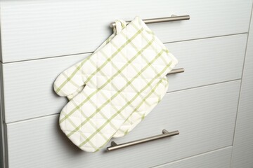 Oven glove and potholder hanging on handle of cabinet in kitchen