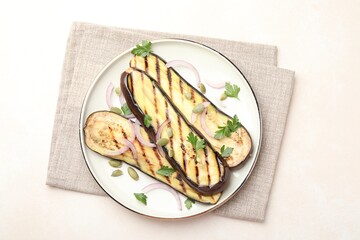 Slices of grilled eggplant, parsley, pumpkin seeds and onion on white table, top view