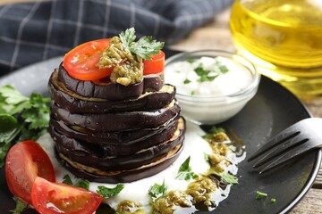 Tasty grilled eggplant slices with tomatoes, pesto and yoghurt on wooden table, closeup