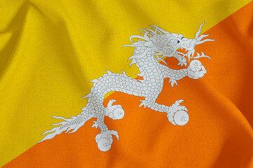 flag of the Kingdom of Bhutan with a white dragon and two triangles of yellow and orange on a rough canvas with folds