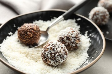 Making tasty chocolate candies with nuts and coconut flakes at light table, closeup
