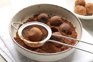Making tasty chocolate candies with cocoa powder at light table, closeup