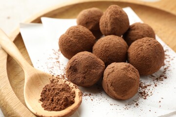 Tasty chocolate candies with cocoa powder and spoon on light table, closeup