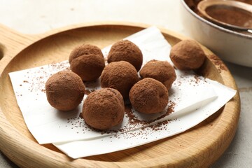 Tasty chocolate candies with cocoa powder on light table, closeup