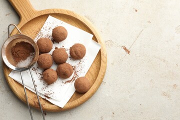 Tasty chocolate candies with cocoa powder and strainer on light table, top view. Space for text