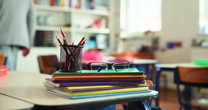 Glasses, books and stationary on desk in classroom for education, learning and knowledge growth. Person, walking and study material to revise lesson, grading homework and academic activity at school