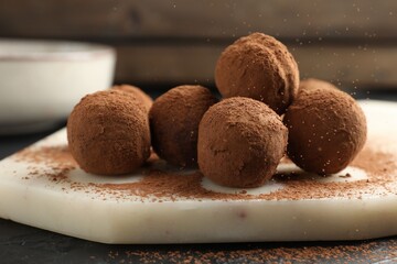 Tasty chocolate candies with cocoa powder on black table, closeup