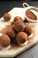 Tasty chocolate candies with cocoa powder on black table, closeup