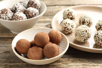 Tasty chocolate candies with cocoa powder, coconut flakes, nuts and sesame seeds on wooden table,...