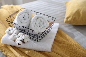 Clean towels, metal basket and cotton flowers on bed linens, closeup