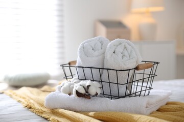 Clean towels, metal basket and cotton flowers on bed linens at home, closeup