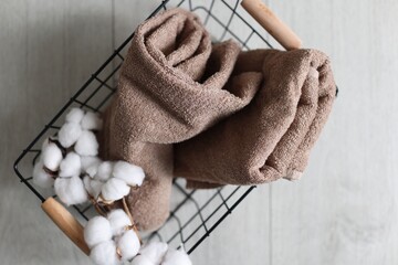 Clean towels and cotton flowers in metal basket on light wooden floor, top view