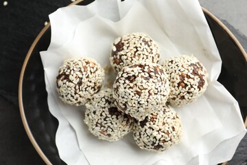 Tasty chocolate candies with nuts and sesame seeds in bowl on table, above view