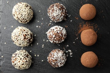 Tasty chocolate candies with cocoa powder, nuts, coconut flakes and sesame seeds on black table,...