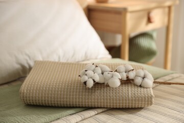 Folded towel and cotton flowers on bed linens at home, closeup