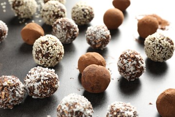 Tasty chocolate candies with cocoa powder, nuts, coconut flakes and sesame seeds on grey table, closeup