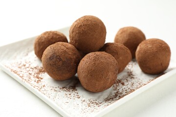Tasty chocolate candies with cocoa powder on white table, closeup
