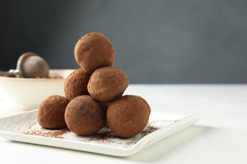 Tasty chocolate candies with cocoa powder on white table, closeup. Space for text