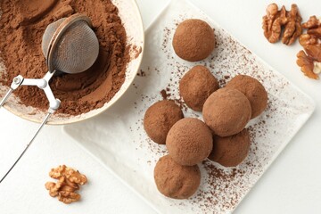 Tasty chocolate candies with cocoa powder and walnuts on white table, flat lay