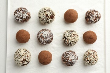 Tasty chocolate candies with cocoa powder, nuts and sesame seeds on white table, top view