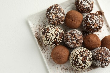 Tasty chocolate candies with cocoa powder, nuts and sesame seeds on white table, top view. Space for text