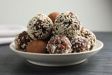 Tasty chocolate candies with cocoa powder, nuts and sesame seeds on black textured table, closeup