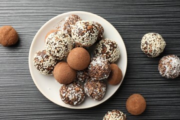 Tasty chocolate candies with cocoa powder, nuts and sesame seeds on black textured table, flat lay