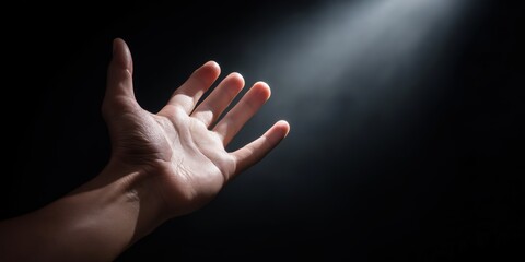 Reaching hand in spotlight against dark background