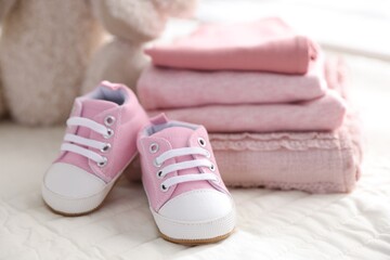Stack of clean baby clothes and shoes on bed linens, closeup