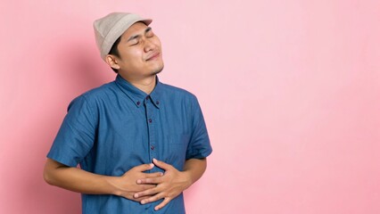 Close Up of Peaceful Young Asian Man in Blue Shirt Holding Stomach with Relief Expression
