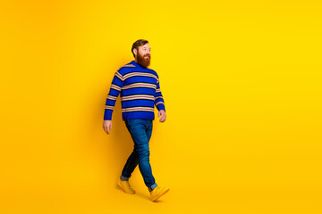 Fototapeta premium Confident young man in a vibrant striped sweater walking against a bright yellow background with stylish flair